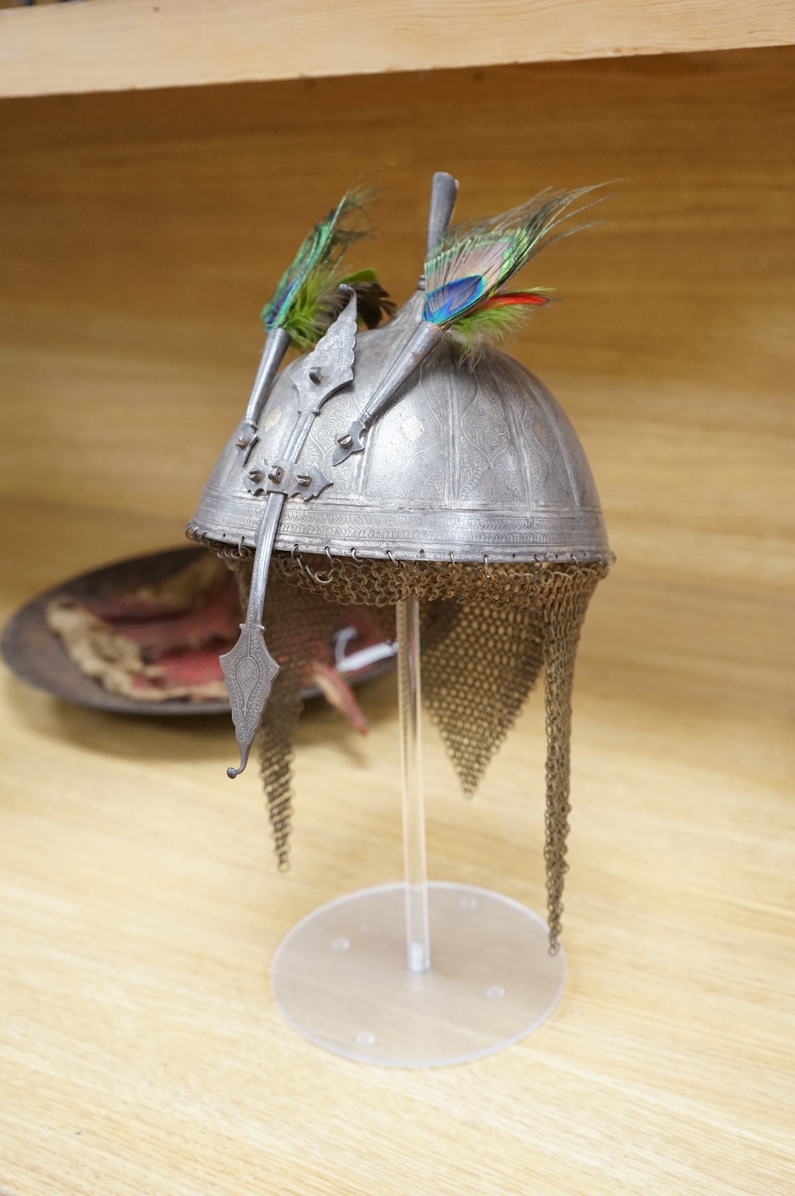 A mid to late 19th century Indian helmet and matching shield, covered with silver koftgari decoration, the helmet with sliding nasal bar and twin plume sockets surmounted by a third plume socket, the skull fluted like a